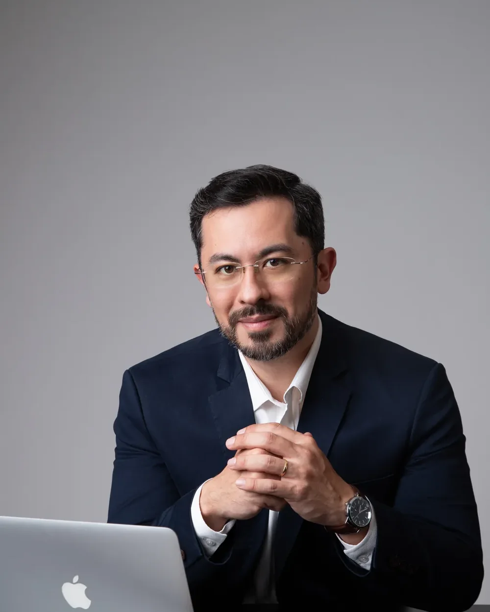 Retrato de homem de óculos e blazer azul-marinho diante de um notebook