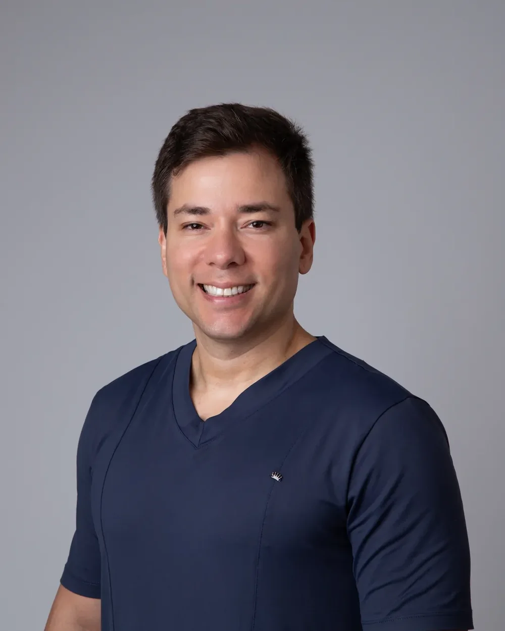 Retrato de homem sorrindo com roupa azul-marinho diante de fundo cinza