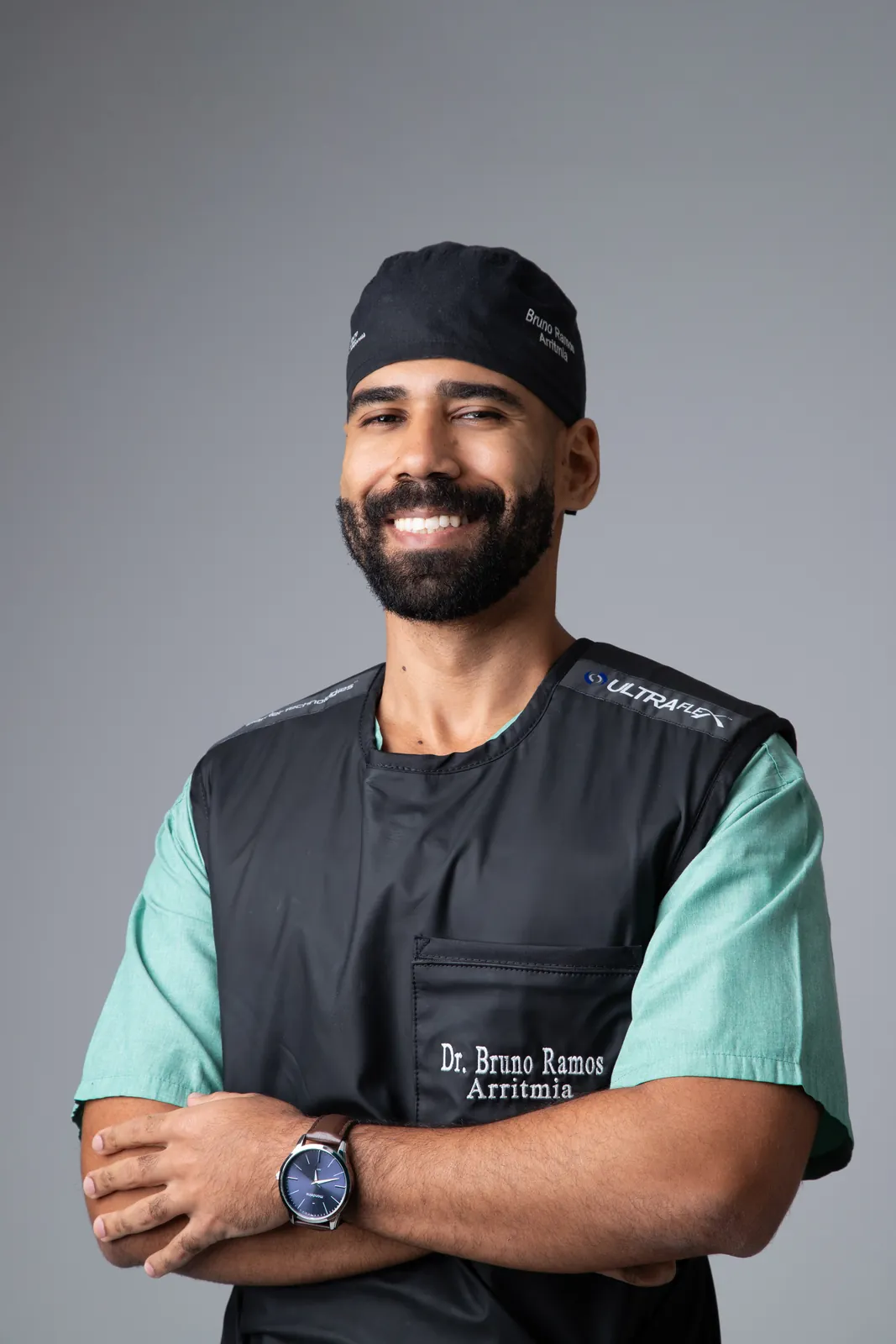 Retrato corporativo de médico sorrindo com roupa cirúrgica verde e braços cruzados