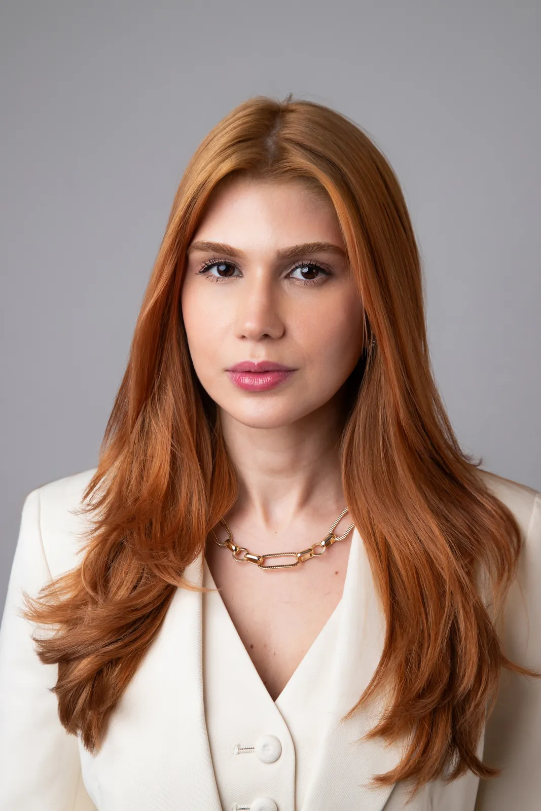 Retrato profissional de mulher ruiva com blazer branco sobre fundo cinza